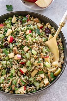 an apple and quinoa salad in a bowl with a wooden spoon next to it