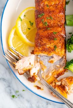 a plate with fish, broccoli and lemon wedges on it next to a fork