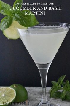 a close up of a martini in a glass with limes and basil on the side