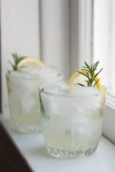 two glasses filled with ice and lemon on top of a window sill