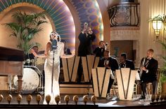 a woman standing on top of a stage in front of a piano and other people