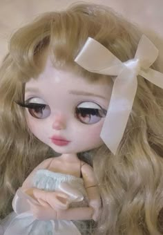 a close up of a doll with long blonde hair and big eyes wearing a white dress