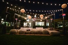 an outdoor seating area is lit up with lights and pillows on the grass at night