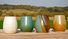 four different colored vases sitting on top of a wooden table next to each other