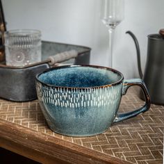 a blue cup sitting on top of a wooden table next to other cups and glasses