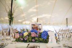 an arrangement of flowers and wine glasses on a table with a photo in the center