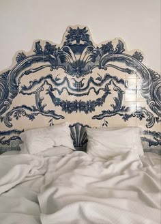 an ornate headboard with white sheets and pillows on a bed in front of a wall