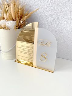 there is a white vase with flowers in it and a card holder on the table