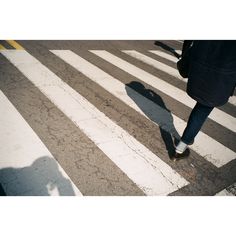 a person walking across a crosswalk in the middle of an intersection, with their shadow on the ground