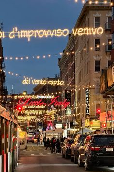 cars parked on the side of a street with lights strung over it and buildings in the background