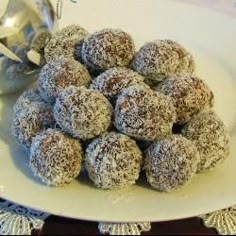 a white plate topped with lots of powdered donuts next to a silver spoon