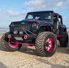 a black jeep parked on top of a sandy beach next to the ocean with pink wheels