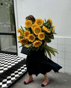 a woman walking down the street carrying a bouquet of sunflowers