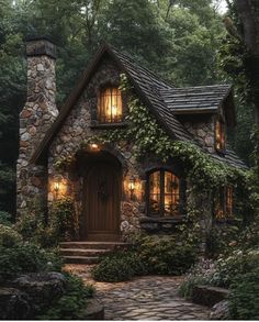 a small stone house surrounded by greenery and trees with lights on in the windows