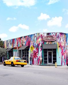 a yellow taxi cab parked in front of a colorful building with graffiti on it's side