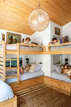 three children are laying on bunk beds in a room with wood ceilinging and white walls