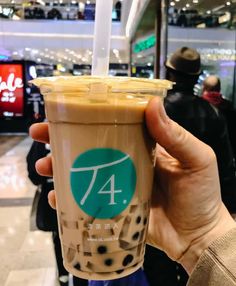 a person holding up a drink in front of an airport terminal with people walking around