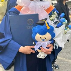 a person in blue graduation gown holding a stuffed animal with flowers on it's lap