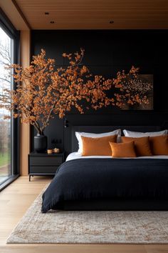 a bedroom with black walls and wooden flooring, large bed surrounded by pillows and orange throw pillows