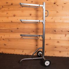 a metal rack with four shelves on wheels in front of a wood paneled wall