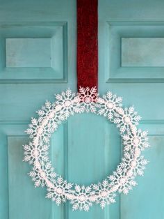 a white snowflake wreath hanging on a blue door with a red ribbon around it