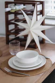 a wooden table topped with white plates and silverware next to a star ornament