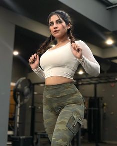 a woman in camo pants and white top posing for the camera with her hands on her hips