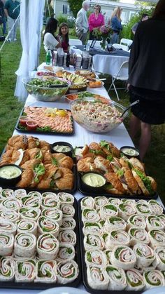 a table full of sandwiches and dips on it's sides at an outdoor party