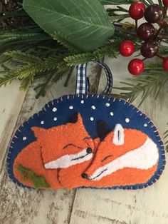 an ornament with two foxes on it next to christmas tree branches and berries