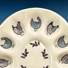 a white platter with chickens and leaves painted on the side, in front of a blue background