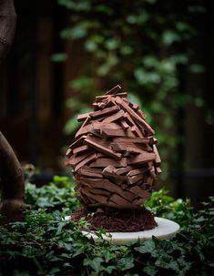 a sculpture made out of wood sitting on top of a white plate surrounded by greenery