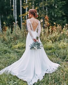 a woman in a wedding dress standing in the grass with her back to the camera