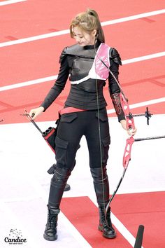 a woman holding a bow and arrow on top of a red carpeted area in front of an arena