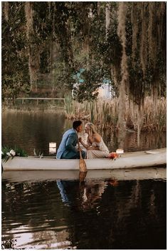 a man and woman kissing in a boat on the water with trees hanging over it