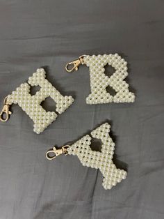 three beaded keychains are sitting on a bed with the letters k and l