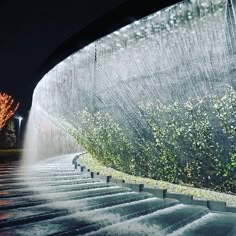 water gushing out from the side of a fountain at night with trees and lights in the background