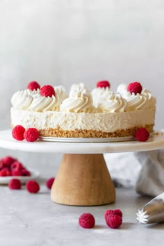 a cake with white frosting and raspberries sitting on top of a table