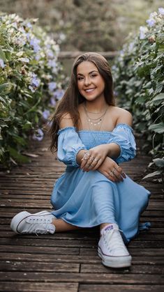 a woman in a blue dress sitting on a wooden walkway