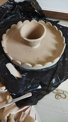 a clay bowl sitting on top of a black piece of plastic next to scissors and other items