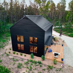 an aerial view of a black cabin in the woods with decking and patio furniture