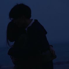 a person standing in front of the ocean at night with their arms around each other