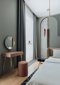 a bedroom with a bed, mirror and side table in front of a curtained window