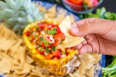 a hand holding a tortilla with fruit and salsa on it next to chips