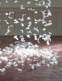 a room filled with lots of white birds flying in the air over a brick floor