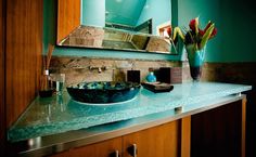 a bathroom counter with a blue bowl on it and flowers in a vase next to the sink