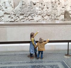 two young children standing in front of a wall with statues on it's sides