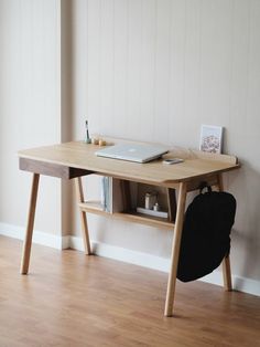 a laptop computer sitting on top of a wooden desk next to a book case and backpack