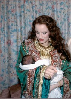 a woman holding a baby wrapped in a green and red blanket with gold trimmings