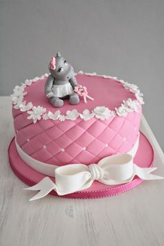 a pink cake decorated with an elephant sitting on top of it's base and ribbon around the edge