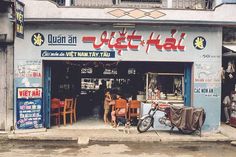 two people sitting at a table in front of a restaurant with a bike parked outside